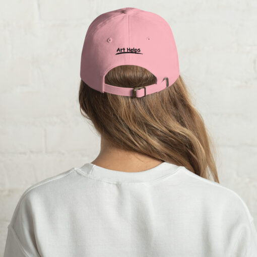 back view of a person wearing a pink "dad" hat featuring the phrase "Art Helps" in black above the adjustment strap