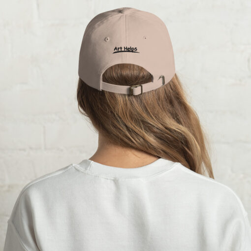 back view of a person wearing a stone-color "dad" hat featuring the phrase "Art Helps" in black above the adjustment strap