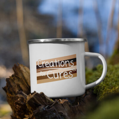 a white enamel mug featuring the Creations for Cures logo over a rectangular graphic made from stripes of diverse skin tones