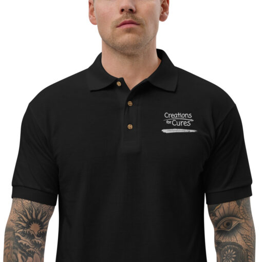 a person wearing a black polo featuring the Creations for Cures logo