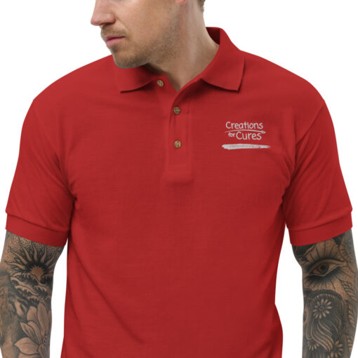 a person wearing a red polo featuring the Creations for Cures logo