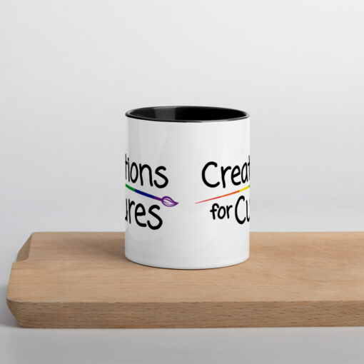 a white ceramic mug with black handle and interior featuring the Creations for Cures logo