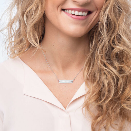 a person wearing a silver bar necklace with the phrase "Art helps" engraved on it