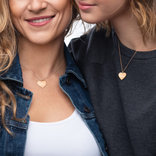two people wearing silver necklaces of a heart with the phrase "Art helps" engraved on them