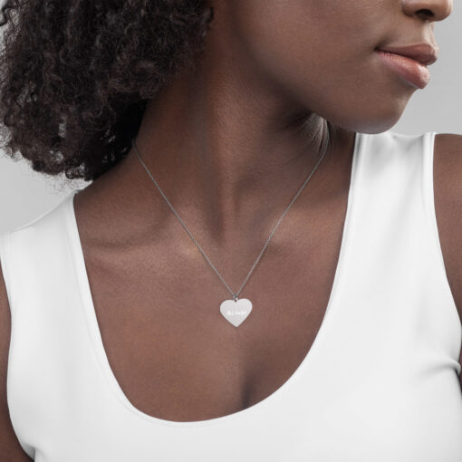 a person wearing a silver necklace of a heart with the phrase "Art helps" engraved on it