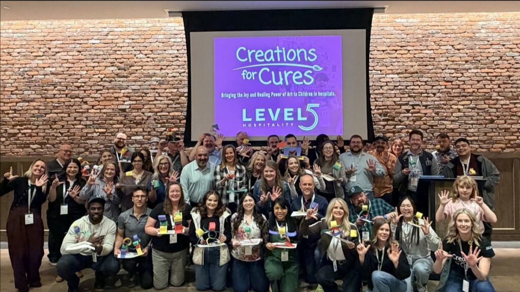 group posing in front of a projector display at the Level5 Hospitality event for Creations for Cures